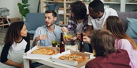 Symbolfoto: Gruppe junge Menschen um einen Tisch mit Pizza in Kartons sitzend