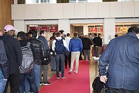 Foto Viele Menschen stehen hintereinander auf einem roten Teppich