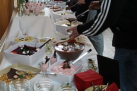 Foto Schalen und Schuesseln auf einem weiß gedeckten Tisch; außerdem Haende, die zu Bestecken greifen