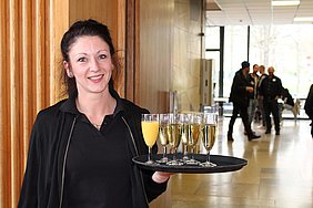 Mitarbeiterin haelt Tablett, auf dem gefuellte Glaeser stehen