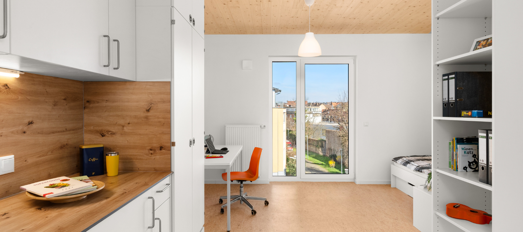 Blick in ein WG-Einzelzimmer mit Spüle, Schreibtisch, Bad und Bett.