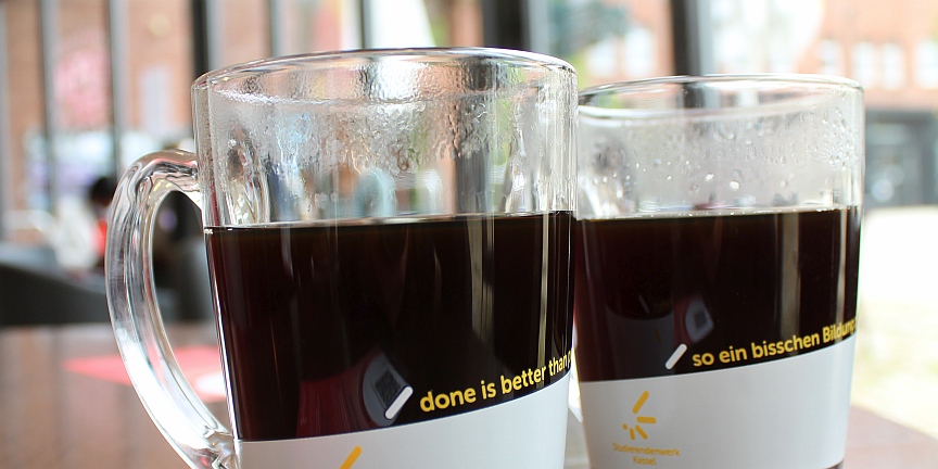 Foto Zwei mit Kaffee gefuellte Glastassen vor Cafeteria-Hintergrund