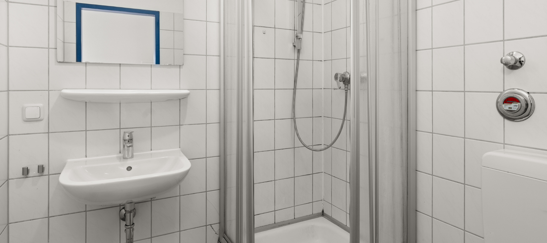 Foto vom Badezimmer der Studiowohnung. Zu sehen sind Waschbecken, Dusche und Fliesen. Alles in Weiß.