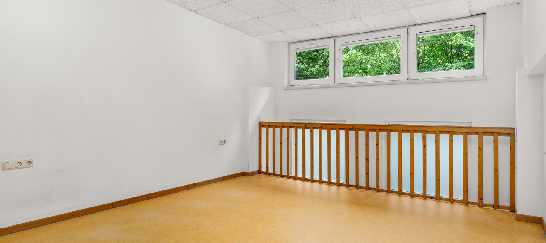 Foto vom Obergeschoss der Studiowohnung. Zu sehen ist eine offene Fläche, die durch ein Geländer begrent wird. Dazu fällt Tageslicht durch die Oberlichter herein.