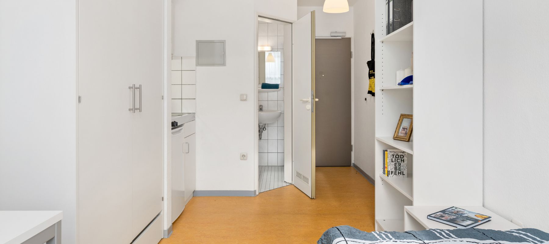 Einzelapartment von innen mit Blick zur Wohnungstüre. Man sieht den Kleiderschrank, die Küchenzeile und die offen stehende Türe zum Badezimmer.