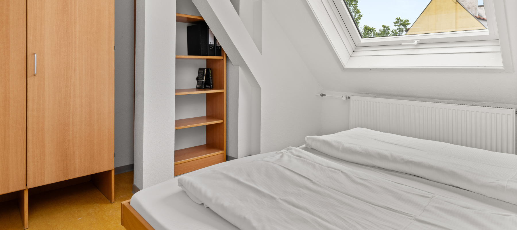 Foto des Familienzimmers. Zu sehen ist das Schlafzimmer mit Doppelbett, Kleiderschrank und Regal. Daneben eine Schräge mit Fenster..