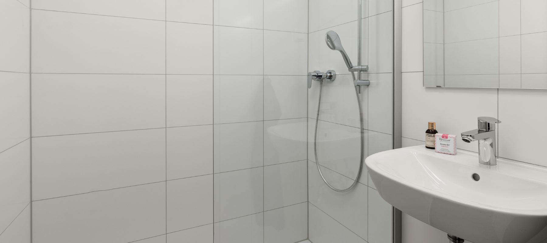 Foto des Familienzimmers. Zu sehen ist das Badezimmer mit Dusche, Waschbecken und Toilette, alles weiß gefliest.