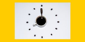 Symbol-Grafik: Weisses Zifferblatt einer Uhr vor gelbem Hintergrund, volle Kaffeetasse in der Mitte, Henkel und Kaffeeloeffel als Zeiger auf 8 Uhr Symbol-Grafik: Weisses Zifferblatt einer Uhr vor gelbem Hintergrund, volle Kaffeetasse in der Mitte, Henkel und Kaffeeloeffel als Zeiger auf 8 Uhr